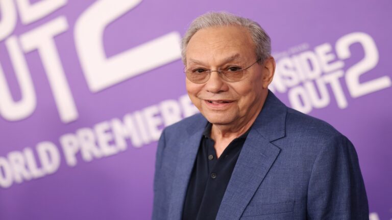 elderly man in a suit with a purple background behind him.