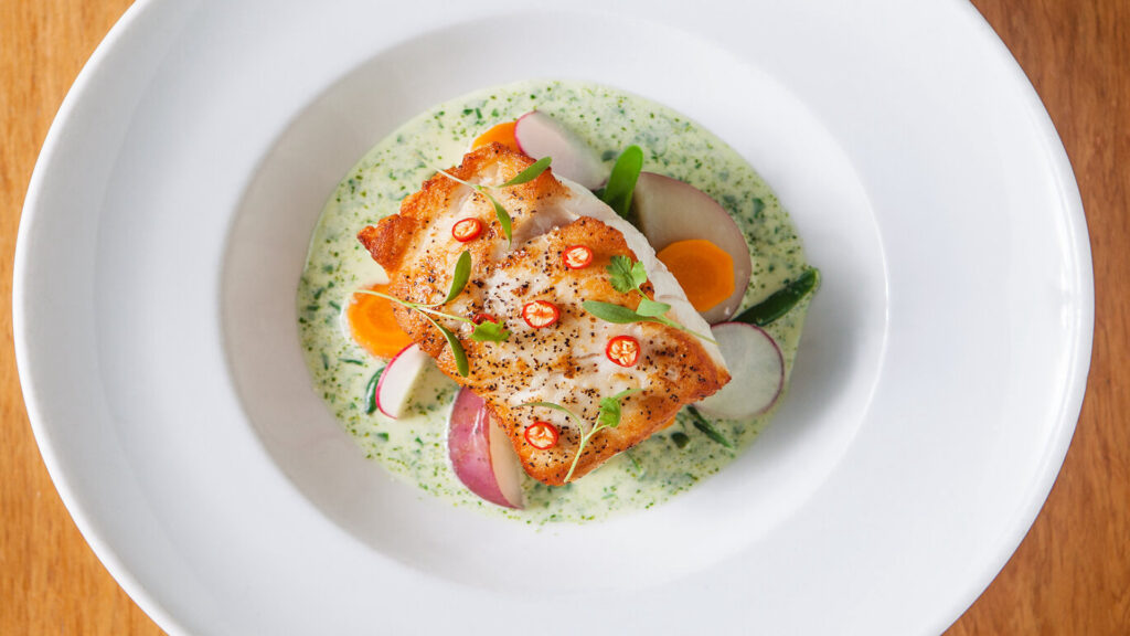 Fish decorated with micro greens and herbs on a white plate.